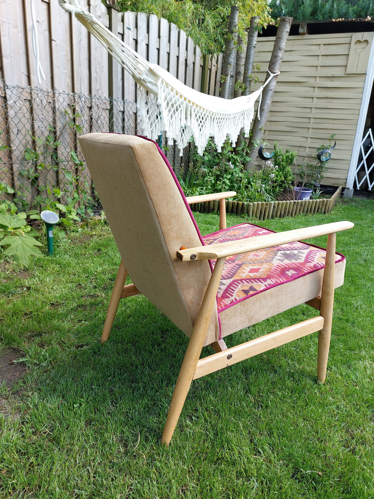 Vintage Sessel neu gepolstert im Boho-Stil, warme Farbtönte, helles Holzgestell, seitliche hintere Ansicht im Garten