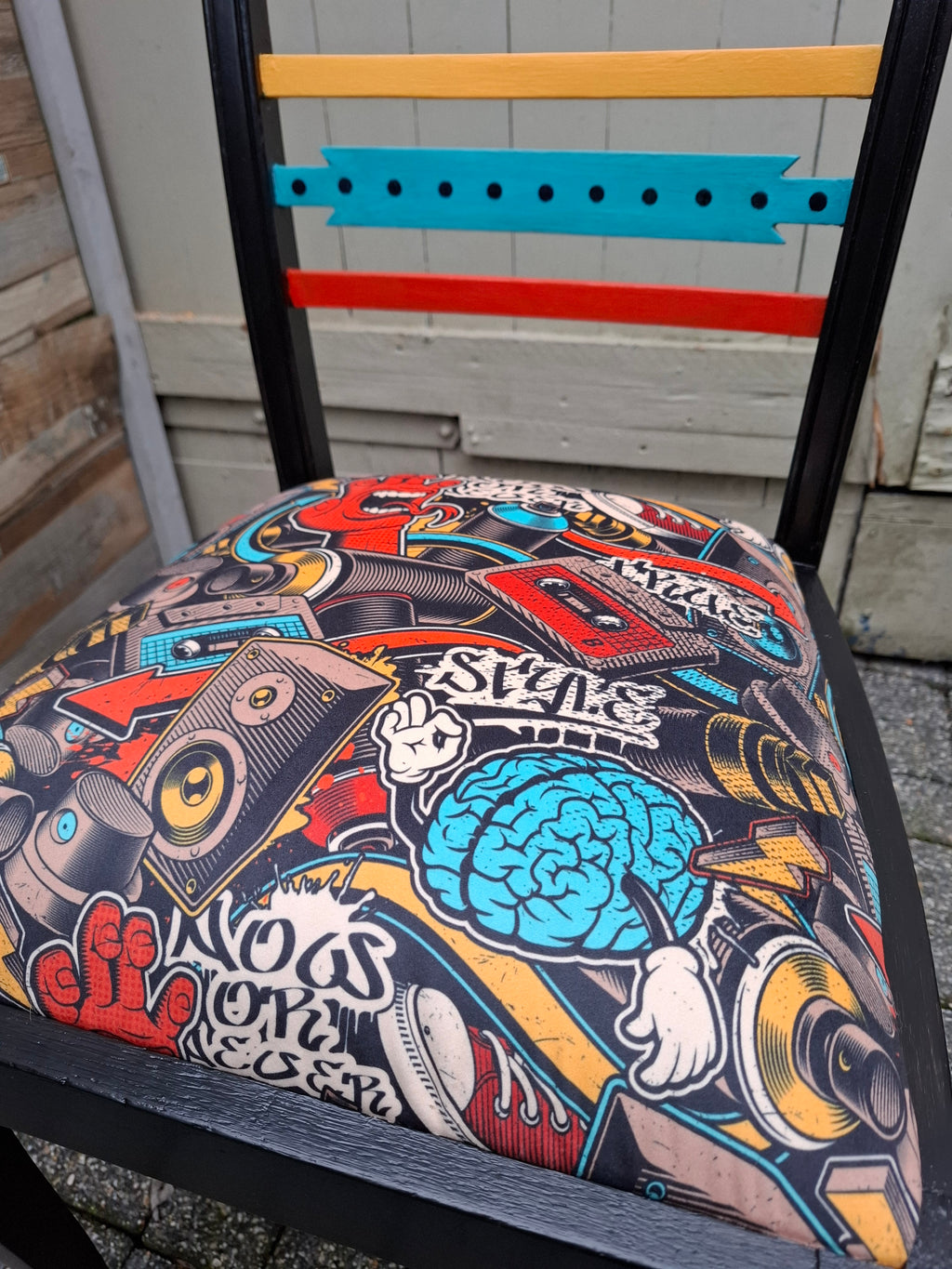 Alter Stuhl komplett aufgearbeitet, schwarzes Holzgestell mit gelben, roten und türkisen Akzenten auf der Rückenlehne, Sitz mit Veloursstoff bezogen mit einem Graffitimuster, Detailansicht Polsterstoff