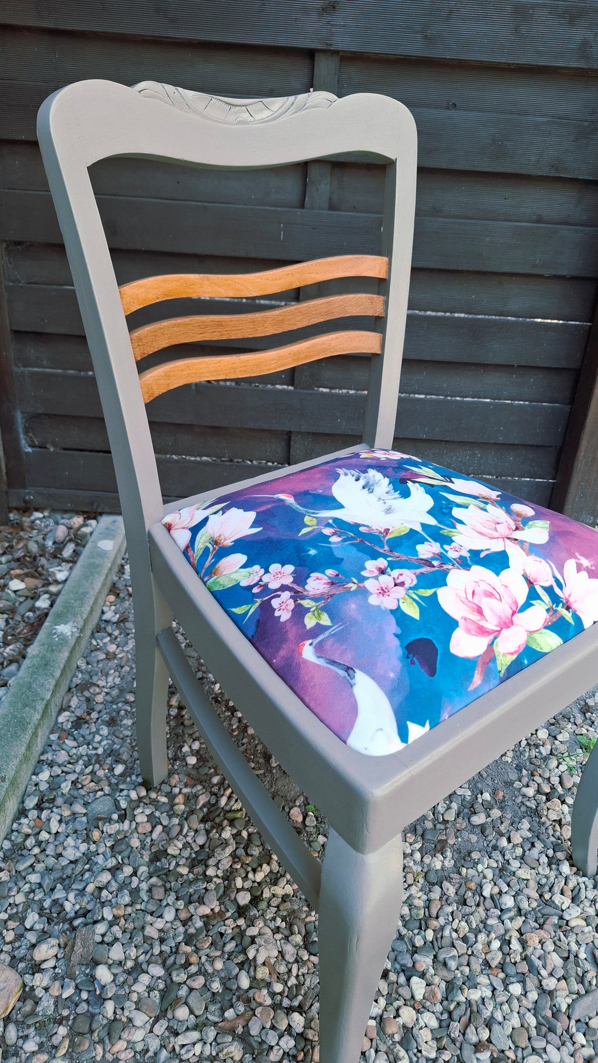Alter Stuhl komplett aufgearbeitet, hellgraues Holzgestell mit naturbelassenen Holdetails auf der Rückenlehne, Sitz mit Veloursstoff bezogen mit Blumen und Kranichmuster, Seitenansicht mit Fokus auf den Sitz