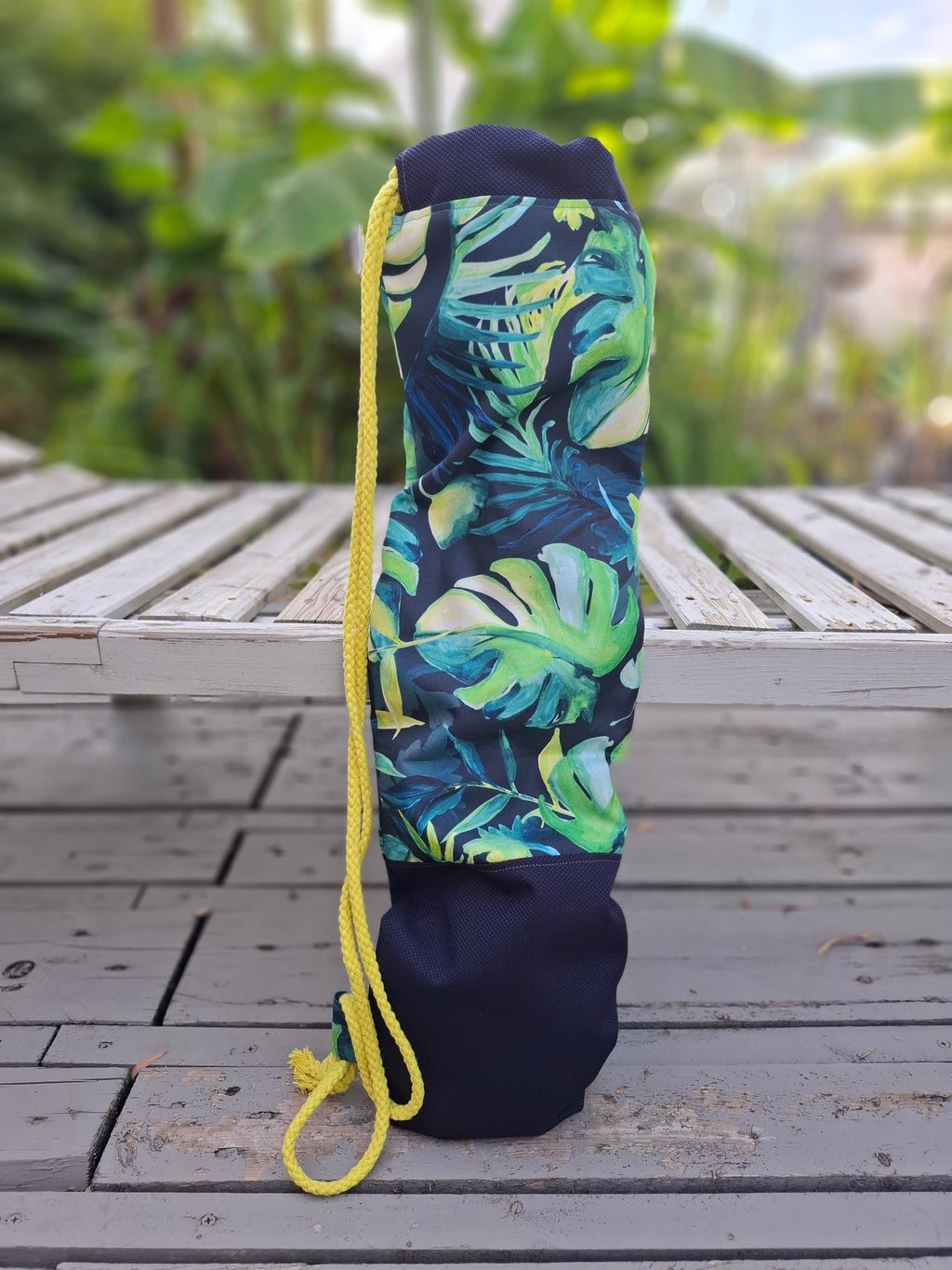 Kellentasche für Saunakellen, oben blau-grünes Muster mit Monstera und anderen Dschungelblättern, unten marineblauer Stoff mit einem Things Outside The Box Lederetikett. Gelbe Kordel. Ansicht von hinten