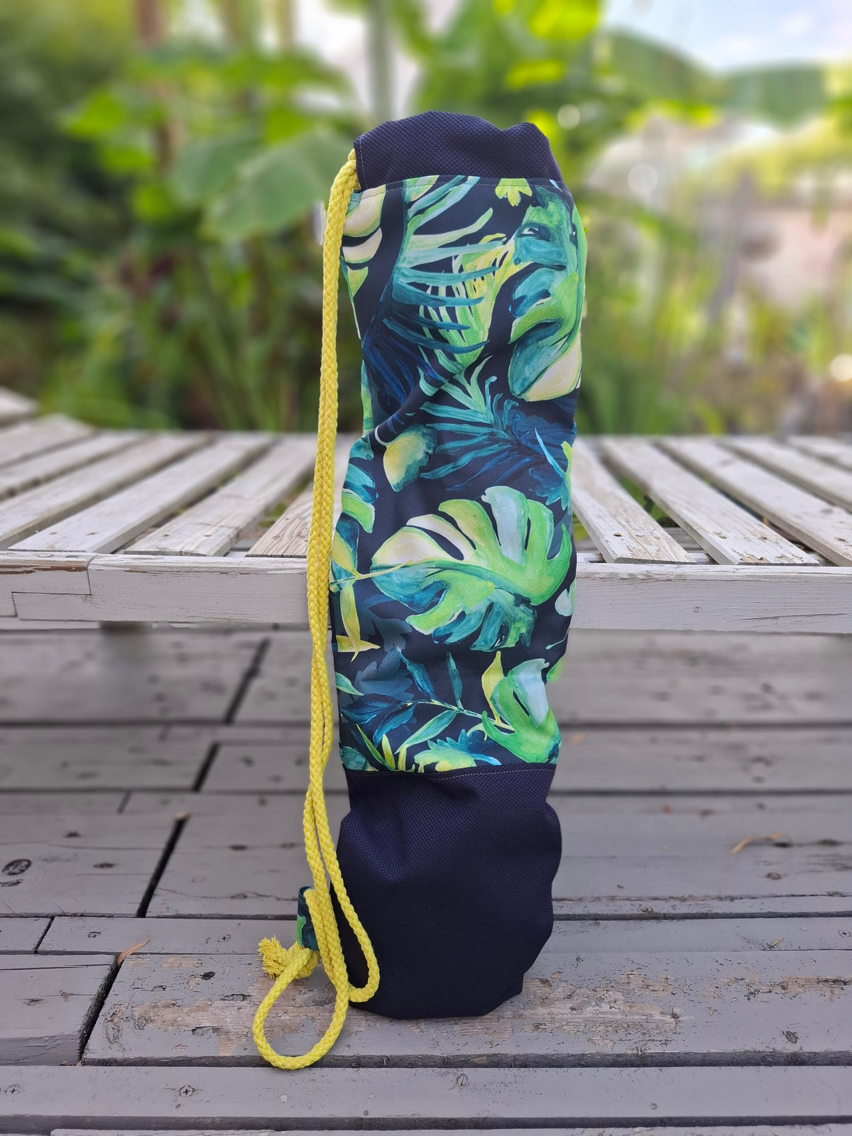 Kellentasche für Saunakellen, oben blau-grünes Muster mit Monstera und anderen Dschungelblättern, unten marineblauer Stoff mit einem Things Outside The Box Lederetikett. Gelbe Kordel. Ansicht von hinten