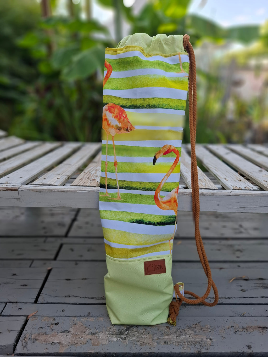 Kellentasche für Saunakellen, oben gelb-grün-weiß gestreiftes Muster mit orangen Flamingos, unten pistaziengüner Stoff mit einem Things Outside The Box Lederetikett. Vorderansicht