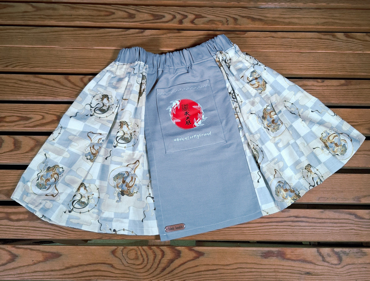 Hanzo Aufguss Art Kilt für Saunameister, japanisches Raijin&Fujin Muster beige-grau, vorne ein hellgrauer Streifen mit einer kleinen Tasche drauf, auf der Tasche das Hanzo Logo, unten ein kleines Logoetikett von Tiröwiki, Vorderansicht Gesamtansicht