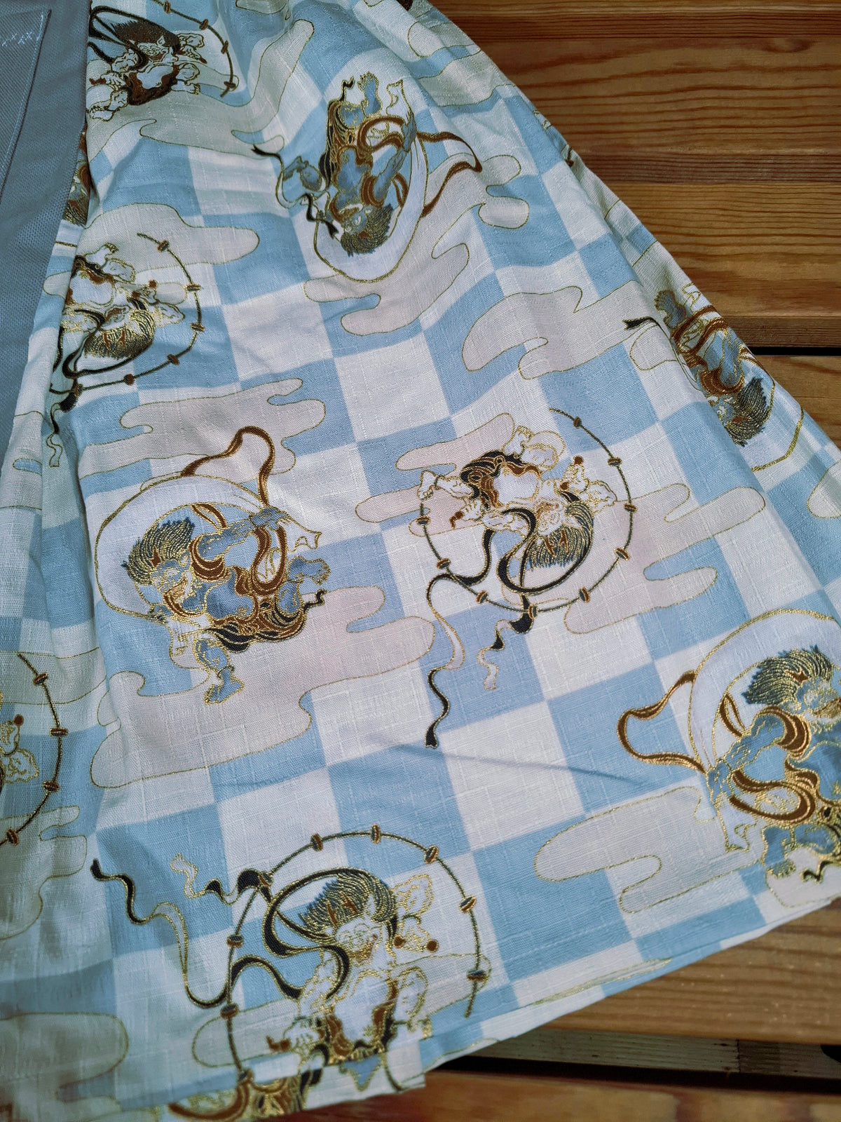 Hanzo Aufguss Art Kilt für Saunameister, japanisches Raijin&Fujin Muster beige-grau, vorne ein hellgrauer Streifen mit einer kleinen Tasche drauf, auf der Tasche das Hanzo Logo, unten ein kleines Logoetikett von Tiröwiki, Detailansicht Stoff