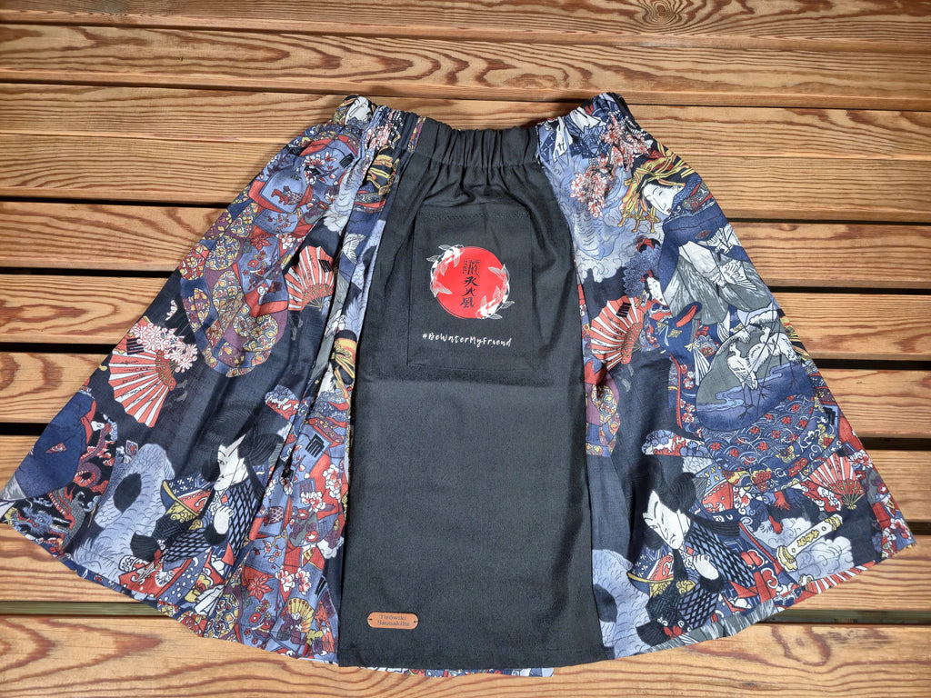 Hanzo Aufguss Art Kilt für Saunameister, japanisches Muster mit Samuraj, Kranichen und Fächern, vorne ein schwarzer Streifen mit einer kleinen Tasche drauf, auf der Tasche das Hanzo Logo, unten ein kleines Logoetikett von Tiröwiki, Vorderansicht Gesamtansicht