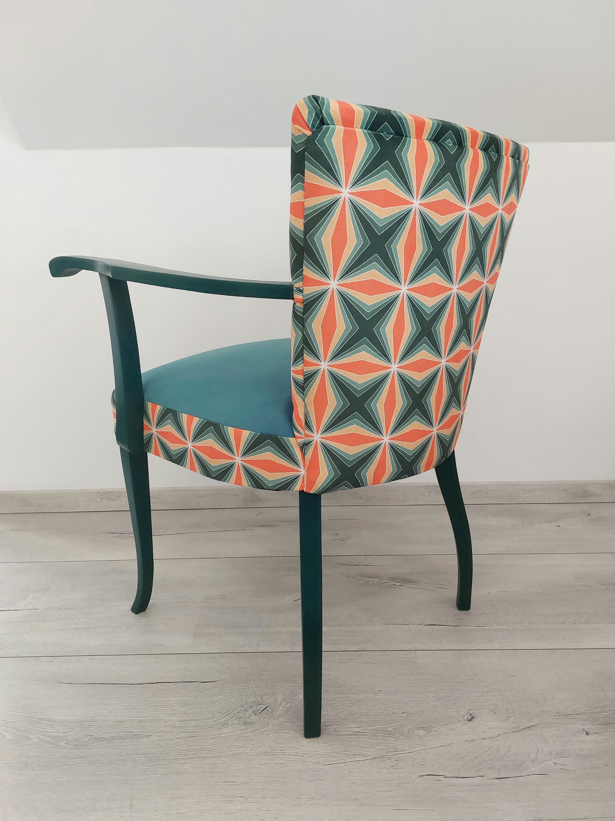 Bunter Vintagestuhl mit Armlehnen, Sitz blau gepolstert, Retro-Muster blau orange, dunkelblaues Holzgestell, Seitenansicht links von hinten