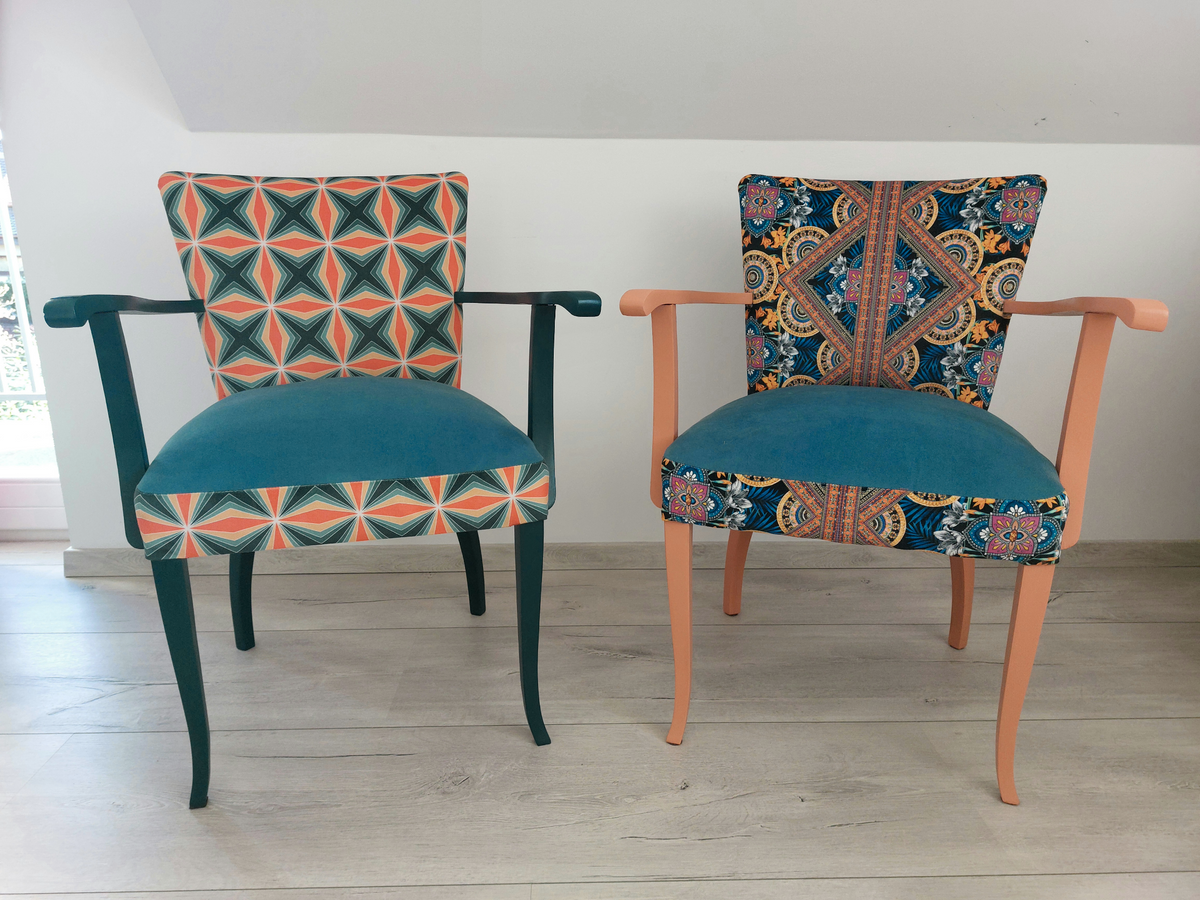 2 bunte Vintagestühle mit Armlehnen, Sitze blau gepolstern, links Retro-Muster blau orange, dunkelblaues Holzgestell, rechts Orient-Muster blau-orange, helloranges Holzgestell, Frontansicht