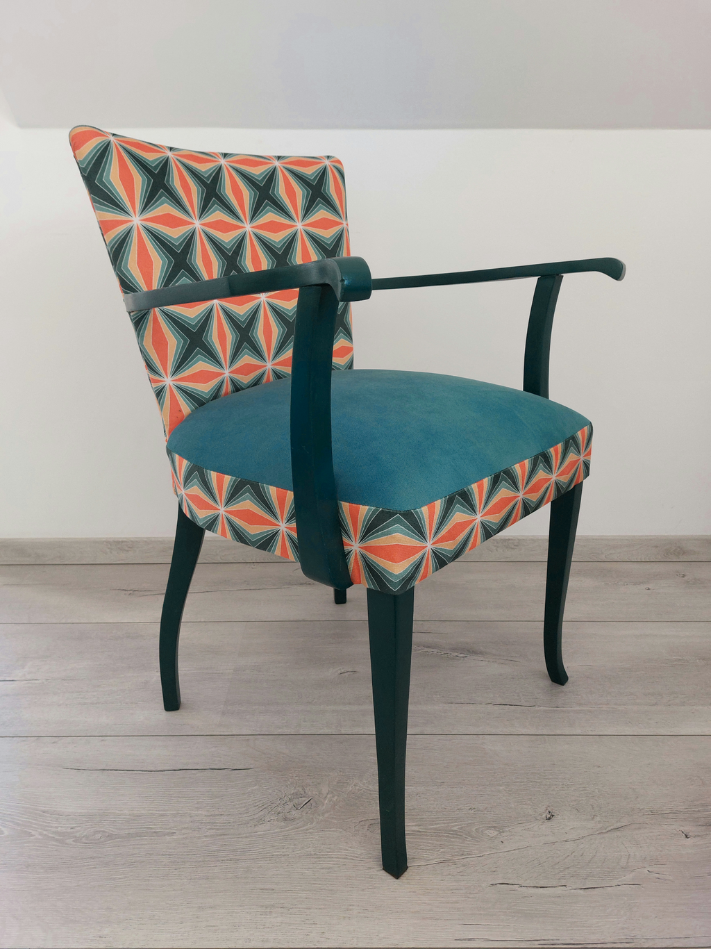 Bunter Vintagestuhl mit Armlehnen, Sitz blau gepolstert, Retro-Muster blau orange, dunkelblaues Holzgestell, Seitenansicht rechts Front